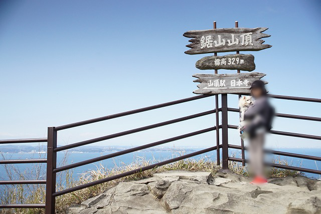 鋸山山頂、標高329m、左 山頂駅、右 日本寺と書かれた看板の前にワンコを抱いて立つ人の写真