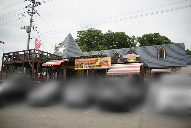 古いアメリカ風の建物の写真。建物には店の名前と、それより目立つ字で「BIG HOT DOG HAMBURGER」と書かれている