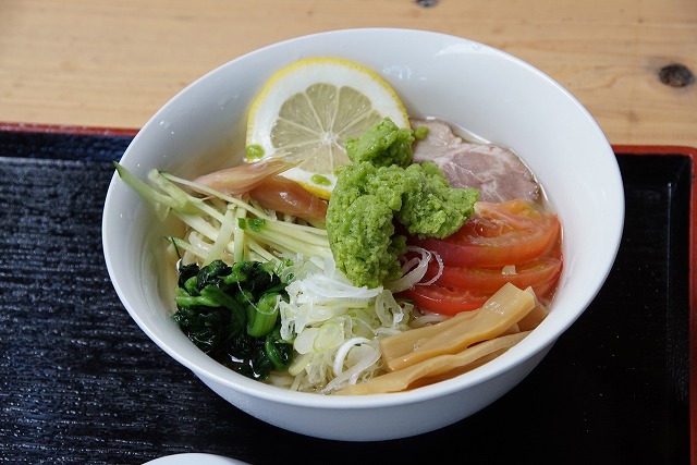 ラーメンの写真。麺の上には、トマト、メンマ、チャーシュー、ミョウガ、ほうれん草、キュウリ、レモンと、薄緑色の粗いペースト状のものがのっています