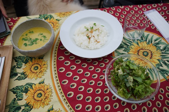 ひまわりの柄のテーブルクロスに置かれたカレーセットの写真。ご飯にもあらかじめ、フライド・オニオンかなにかなどのトッピングがのっている