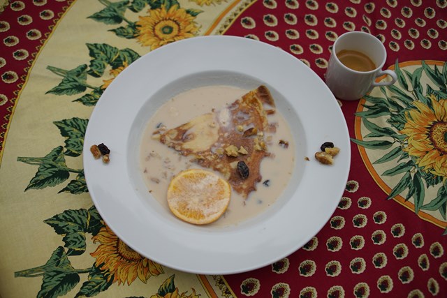 Foto de una crepe bañada en sopa de aspecto dulce. Hay frutos secos en los bordes del plato y sobre la crepe.