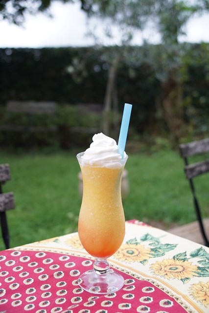 Foto de una bebida de naranja en un vaso transparente vertical. Hay una pajita azul claro insertada.