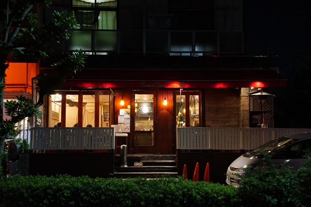 Foto de la "Trattoria Santa Teresa" por la noche. Se aprecia una cálida luz en el interior del restaurante. En el alero está escrito "Trattoria Santa Teresa"