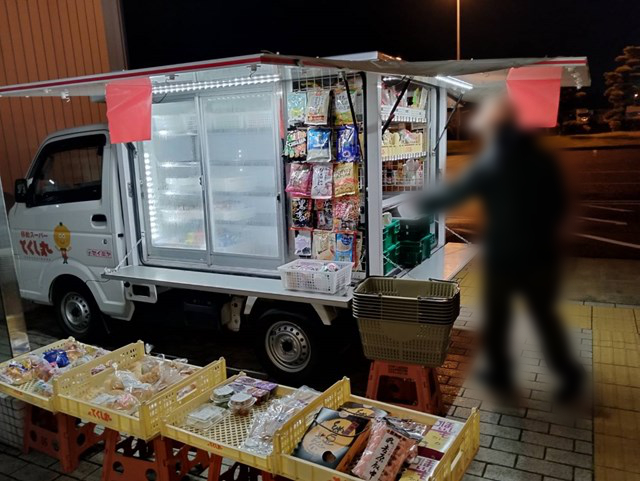 Foto de un coche que vende comidas para llevar y aperitivos en estanterías instaladas en la parte trasera de un camión. Los dos tercios delanteros del coche son un refrigerador. También hay productos alineados junto al coche