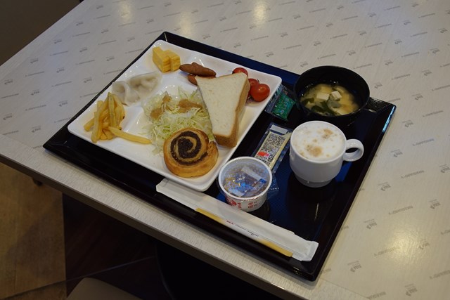 お盆に載せた朝食の写真。載っているのは、食パン、菓子パン、コーヒー、納豆、味噌汁、水餃子、フライドポテト、卵焼き、ウィンナー、ミニトマト、千切り野菜