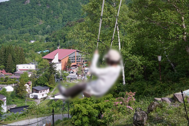 ブランコに乗る人の写真。足下に遠くの建物が見えます
